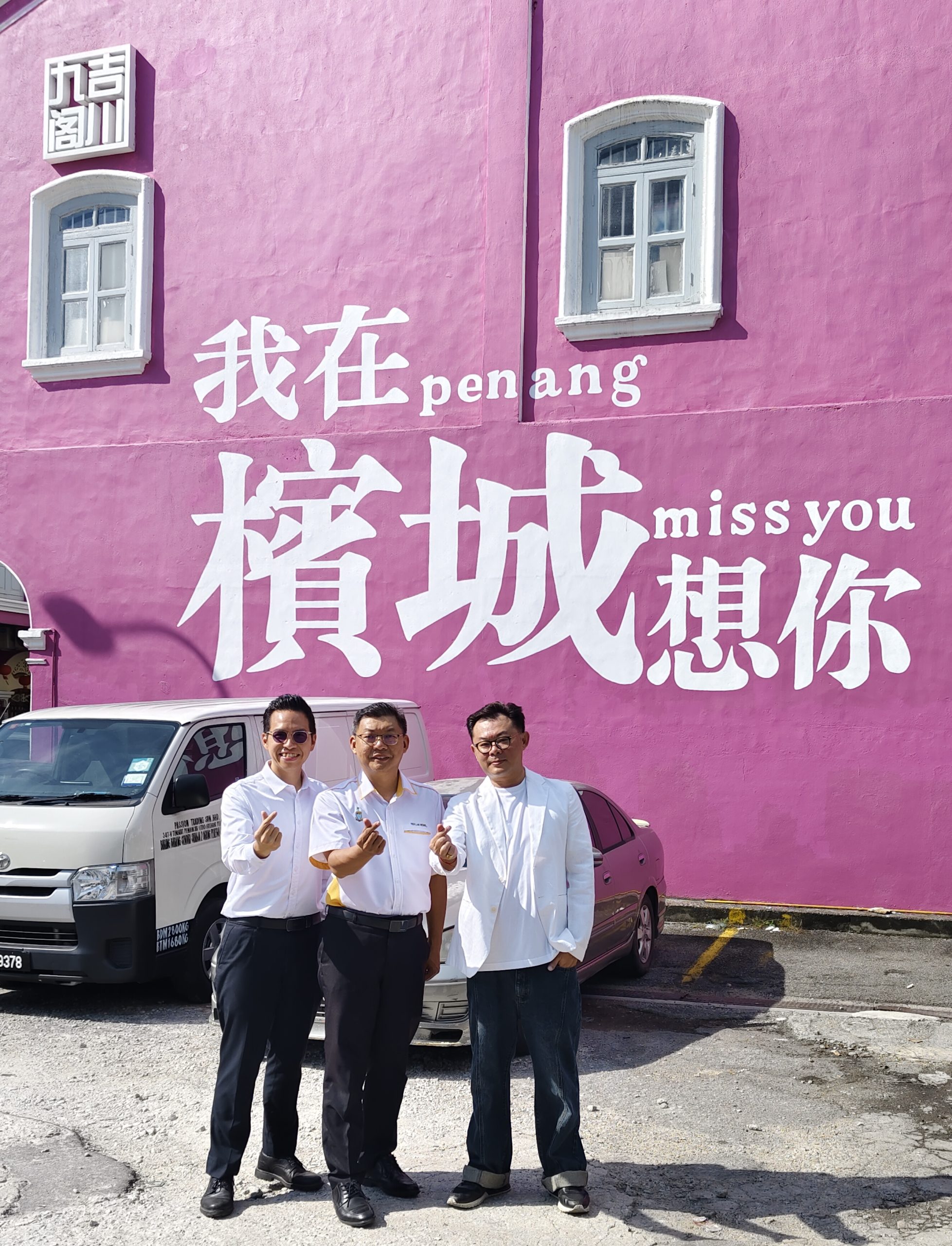 张祥隆(右起)向郑来兴及洪明泉展示绘画在髮绅自家房屋墙上的打卡画面。