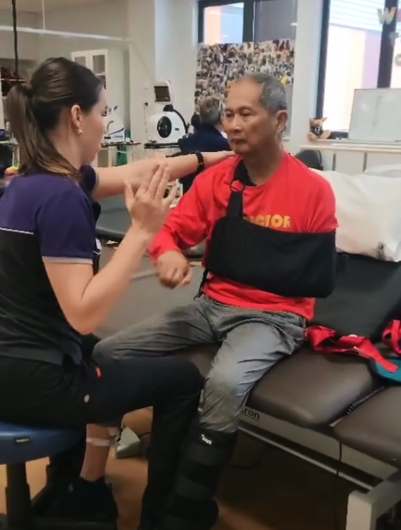 黄达明在一名医护人员的帮助下，做右手部移动与伸展的动作