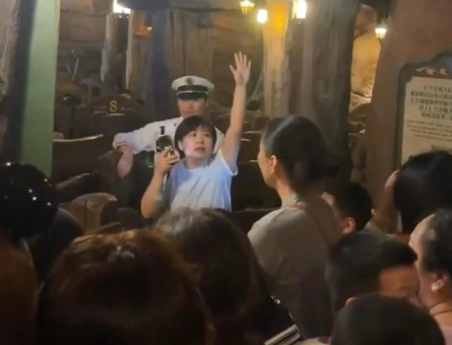 妇女面向人群不断比划手势，期间高喊“大家往前冲！”，企图煽动其余民众冲入游乐设施。（视频截图）