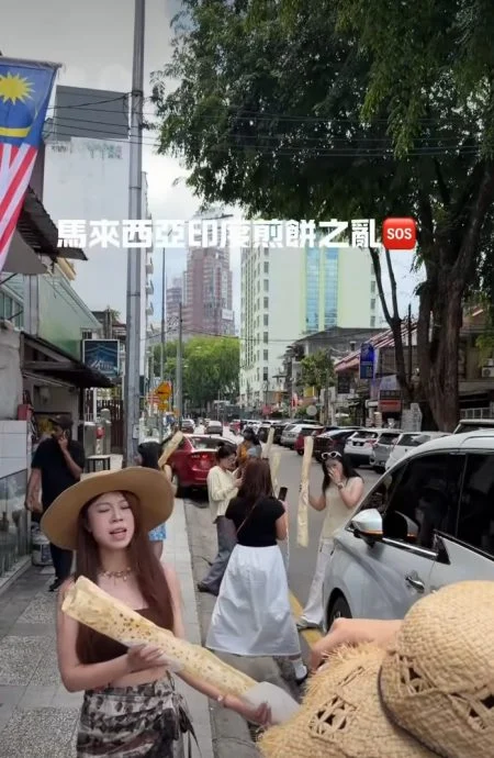 女游客全部站到了店外,远处背景为吉隆坡高楼,手上各握着“一大支”Roti tisu,然后摆起各种姿势拍照。(视频截图)